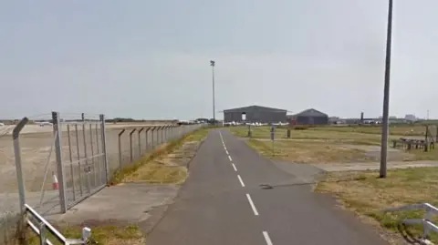 Google A Google maps image of a road leading to a hangar with planes parked up on a runway to the left 