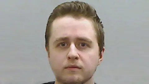 A police-issued photograph of Alexander McCartney - he is looking directly into the camera, and has short brown hair.