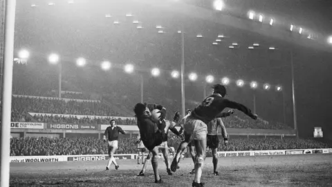 Getty Images A horizontal Phil Parkes holds on to a ball at Goodison Park, surrounded by five Wolves and Everton players. Floodlights illuminate the pitch with a large crowd in the stands 