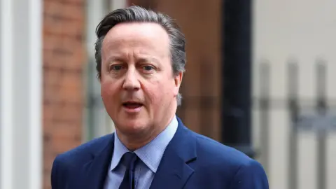 Reuters David Cameron walking out of Downing Street in London. He is wearing a blue blazer, blue tie and a shirt with blue and white stripes.
