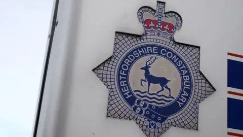 A close-up of the Hertfordshire Police badge on the side of a police building.