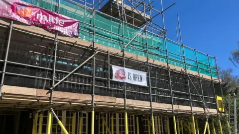 Owen Sennitt/BBC Scaffolding surrounds a building on a bright sunny day with blue skies in the background