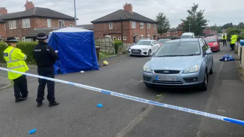 BBC Two police officers look on behind police tape at the scene on Barnard Road.