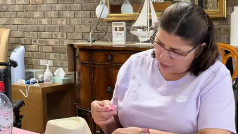 Dina holds a flower petal above her hat as she looks at wear to place it
