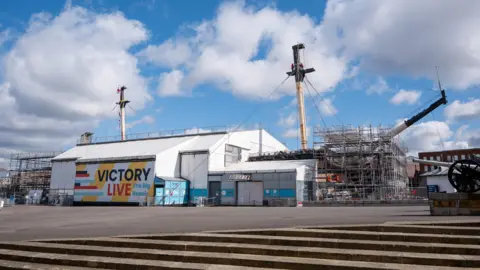 NMRN Scaffolding and temporary buildings erected near the ship. Its masts are visible behind.