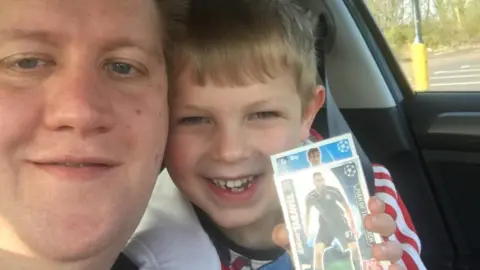 David Bown with his cousin, who is holding a football card. They are both sitting in a car.
