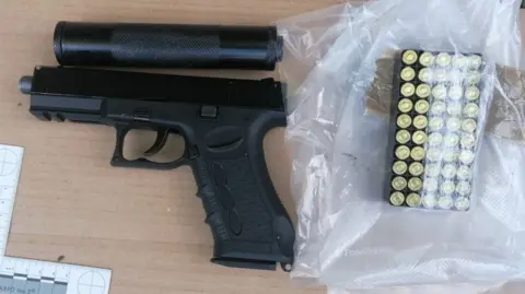 National Crime Agency A black handgun resting on a desk next to ammunition.