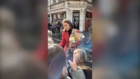 Princess of Wales pictured greeting crowds holding flowers in a red coat 