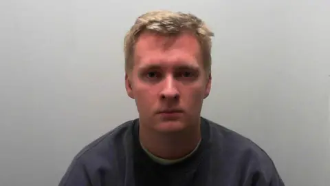 North Yorkshire Police A mugshot of a man in his early 20s with blond hair. He has a serious expression and is wearing a dark grey jumper. 