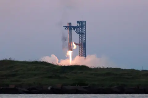 Reuters The booster from the Starship rocket is shown landing between two mechanical arms with flames emitting from its base