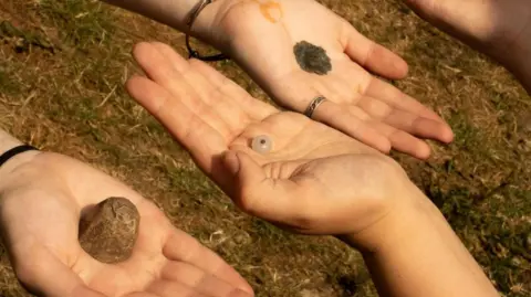 Alexander Jansen/Durham University Three palms stretching out with objects found during the excavation placed on top of them, including two metal pieces and a bead.