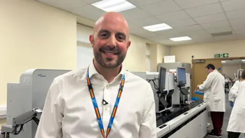 A man smiling whilst standing in a medical lab.