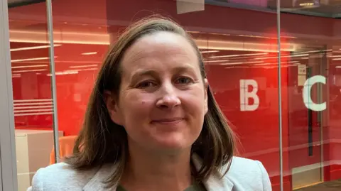 A smiling Camilla Marcus-Dew, co-founder of Amplify Goods, stood in front of a glass wall with the BBC logo reflected on it