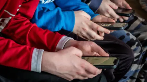 Stock image showing close-up of three pairs of teenagers' hands holding smartphones.