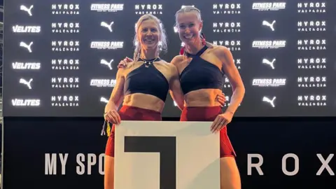 Emma Holmes Two women smiling in fitness gear standing on a podium with their arms around each other