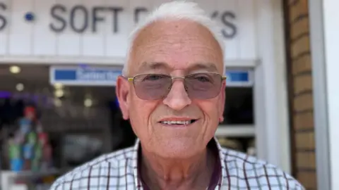 A head and shoulders photograph of Dave Charles. He has white hair and is wearing glasses and a checked shirt.