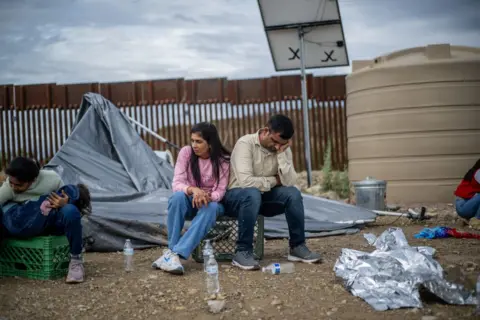 Getty Images Migran yang mencari suaka dari Gujarat di India menunggu untuk ditangkap oleh petugas adat dan perlindungan perbatasan AS setelah menyeberang ke AS pada 25 Juni 2024 di Ruby, Arizona.