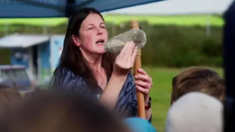 Trust education and outreach manager Caroline Davey showing an ancient axe head to a group of children. 
