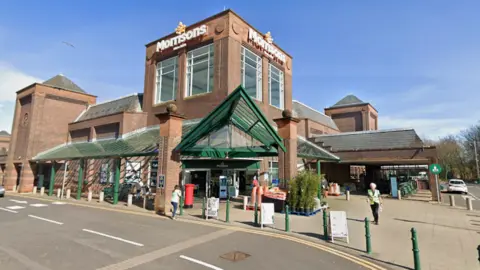 Google A Morrisons supermarket with its sign above the entrance and a couple of people outside