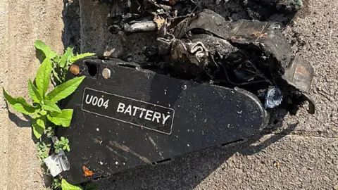 Cardiff Council Black box with U004 battery written on the side lies on the road surrounded by charred debris