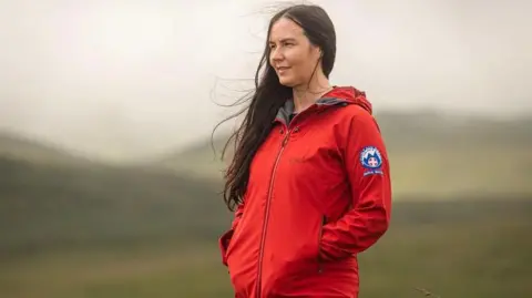 this girl walks Carys Rees, wearing a red jacket, looks out at scenery in Bannau Brycheiniog