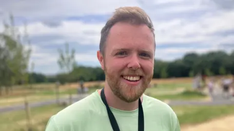 Elizabeth Baines/BBC A man in a green top smiles. Behind him a bike park is blurred.