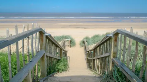 Getty Images Wooden steps leading to a golden sand beach, with the sea in the distance
