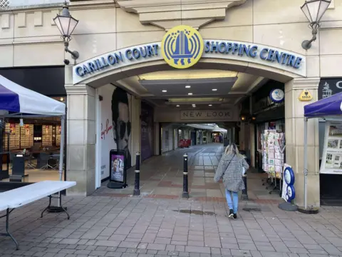 The entrance to the centre from Market Place, with a lone shopper walking in below the Carillon Court sign and bell logo