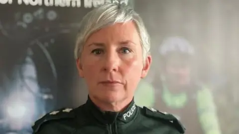 PSNI Ch Insp Yvonne McManus in PSNI uniform standing in front of a policing campaign board. She has short blonde hair. 