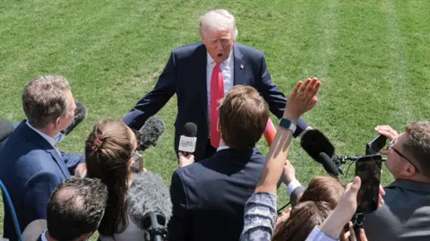 Getty Images US President Donald Trump, wearing a dark suit and red tie, speaks to the media on the South Lawn of the White House