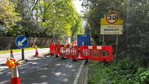 Clare Dutton / BBC Roadworks on a rural road. A sign next to the road reads "Welcome to Bramley please drive carefully".