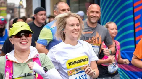 Three women and three men are running in a city centre race. They all wear sportswear and race cards with numbers on.