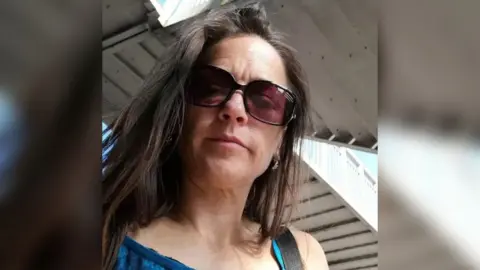 Joanne Sheen has long, dark brown hair and wears sunglasses and a lacey blue, sleeveless top.