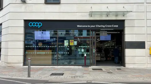 A picture of the outside of the coop in St Helier, with black hoarding and blue lettering making up it's logo. 