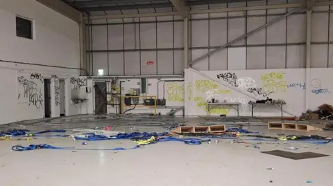 An empty industrial unit has graffiti on the walls and what looks like blue banners on the floor