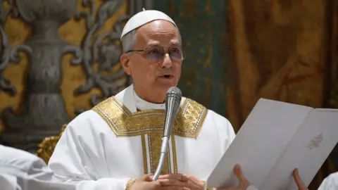Pope Leo XIV speaking into a microphone in his first mass at the Vatican