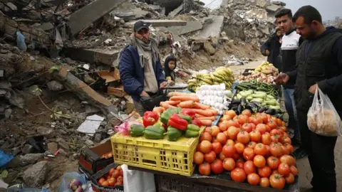 Getty Images A group of Palestinians sets up a small market amid the ruins of destroyed buildings in Gaza's Jabalia refugee camp, selling fresh vegetables and fruit as daily life continues under difficult conditions following the enforcement of a ceasefire agreement on 10 February 2025.