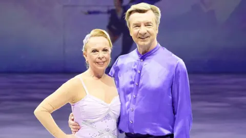 PA Media Jayne Torvill and Christopher Dean pose on the ice on their recent tour - in the latest versions of their purple Bolero costumes.