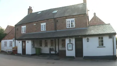 Exterior of a large two-storey pub, with a white washed ground floor and a brick upper floor. 