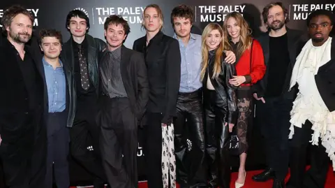 Getty Images Ross Duffer, Gaten Matarazzo, Finn Wolfhard, Charlie Heaton, Jamie Campbell Bower, Joe Keery, Natalia Dyer, Maya Hawke, Matt Duffer, and Caleb McLaughlin in a row, all are in smart clothes on a red carpet