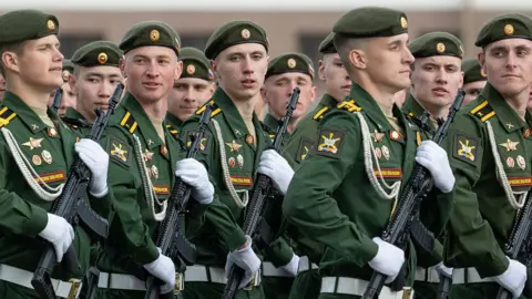 Getty Images Russian soldiers rehearse for parade on Red Square - they are in uniform, holding automatic weapons with white gloves, marching left to right and looking towards the camera.