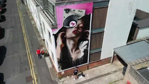 Jake Davis/Upfest A street art mural being painted in Bristol as part of Upfest Presents. It shows a woman's face and a loudspeaker