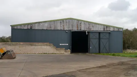 James Towill An old empty hangar building viewed across a paved area