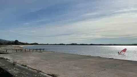 a windsurfer on a reservoir on a sunny day with the concrete banks of the water exposed