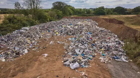 A drone shot of waste in a field- with a soil embankment to the right of the shot. 