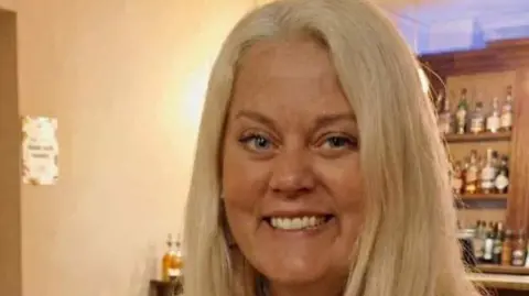 Dorset Police Rebecca French, a blonde haired woman who is stood in front of a drinks cabinet smiling at the camera.