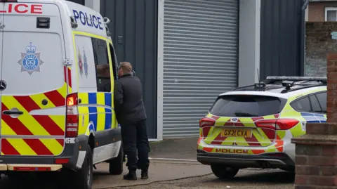 A police car and a police van are parked outside the units in Eastbourne and a man is standing by the van talking to someone inside the vehicle through the window.