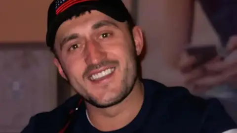 Sali Byberi smiling at the camera wearing a cap backwards and a black T-shirt