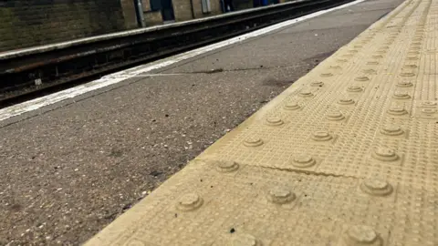 Kit Taylor/BBC Close up image of tactile paving on a train platform edge. 