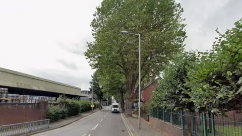 A road is near the bottom of this generic image on the left. A large tree is prominent in the middle of the photo and part of a house is visible to the right of it.